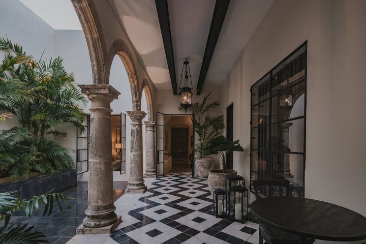 Corredor de arcos de piedra en el patio de una de las casonas de Casonas MX, con piso ajedrezado, plantas y faroles.